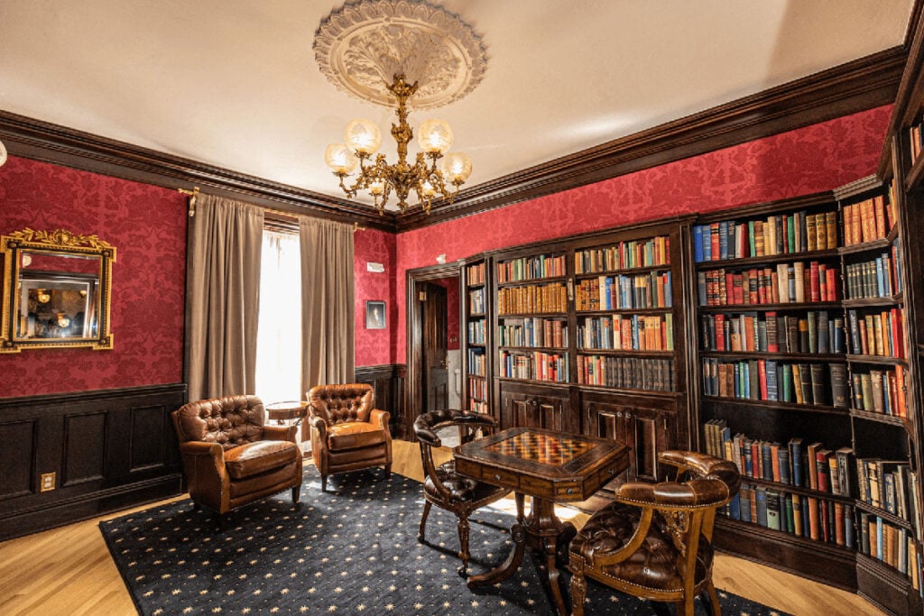 Library with red brocade walls and dark brown trim and shelves