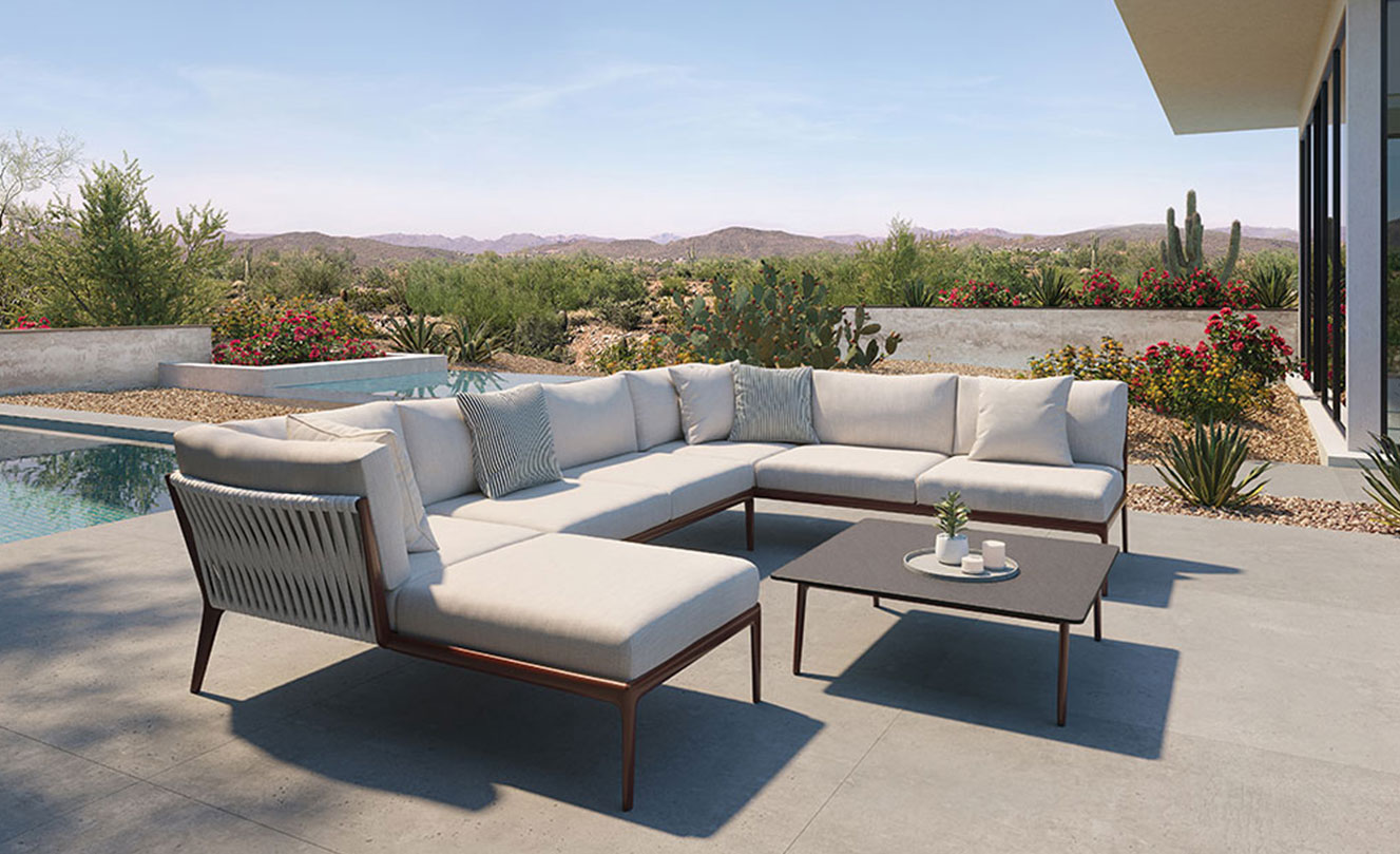 A modern outdoor lounge chair and ottman with grey woven seat and teak frame on an architectural concrete and wood patio with potted cactus