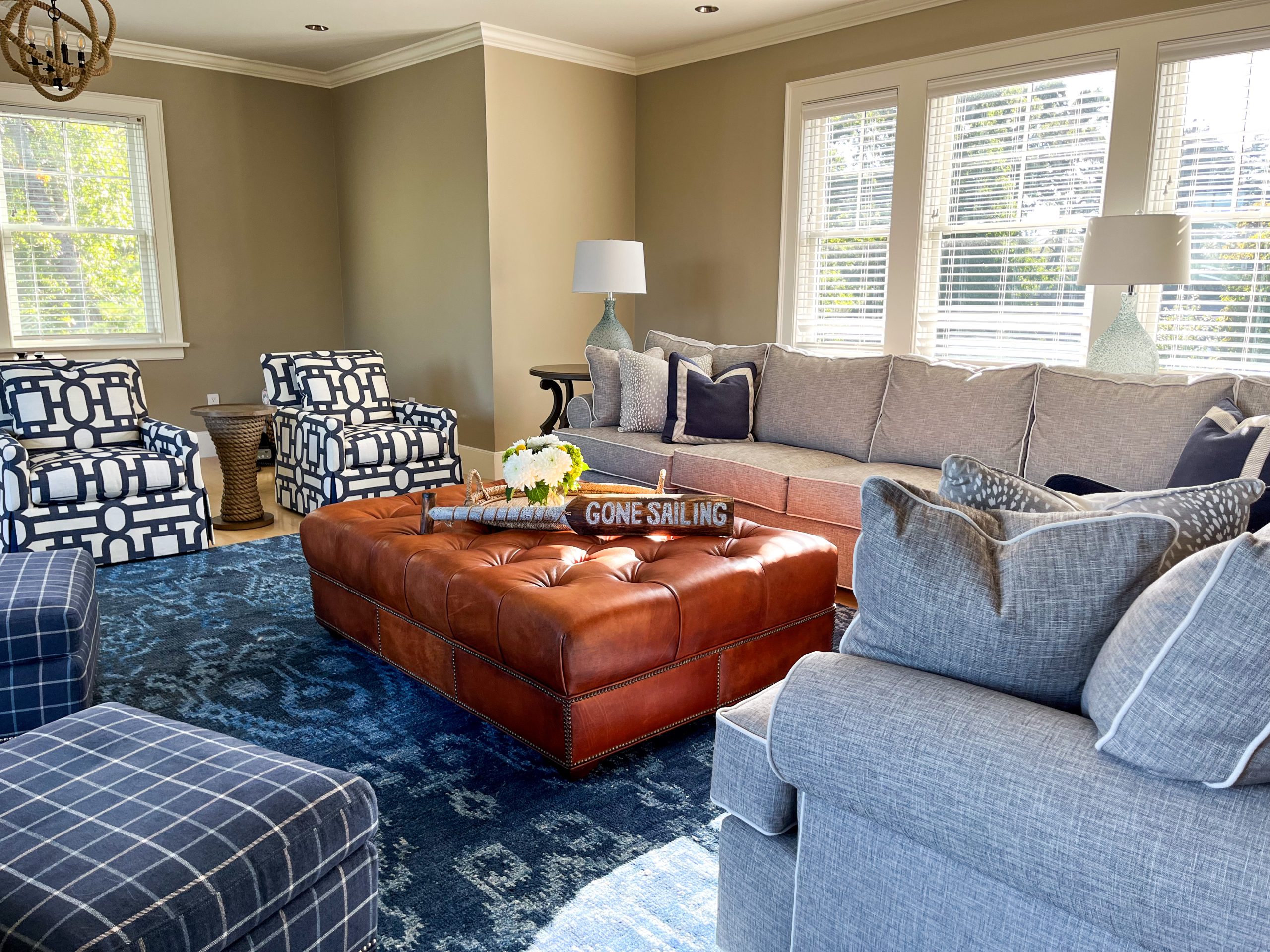 A comfortable living room with grey and blue furnishings and a brown leather ottoman.