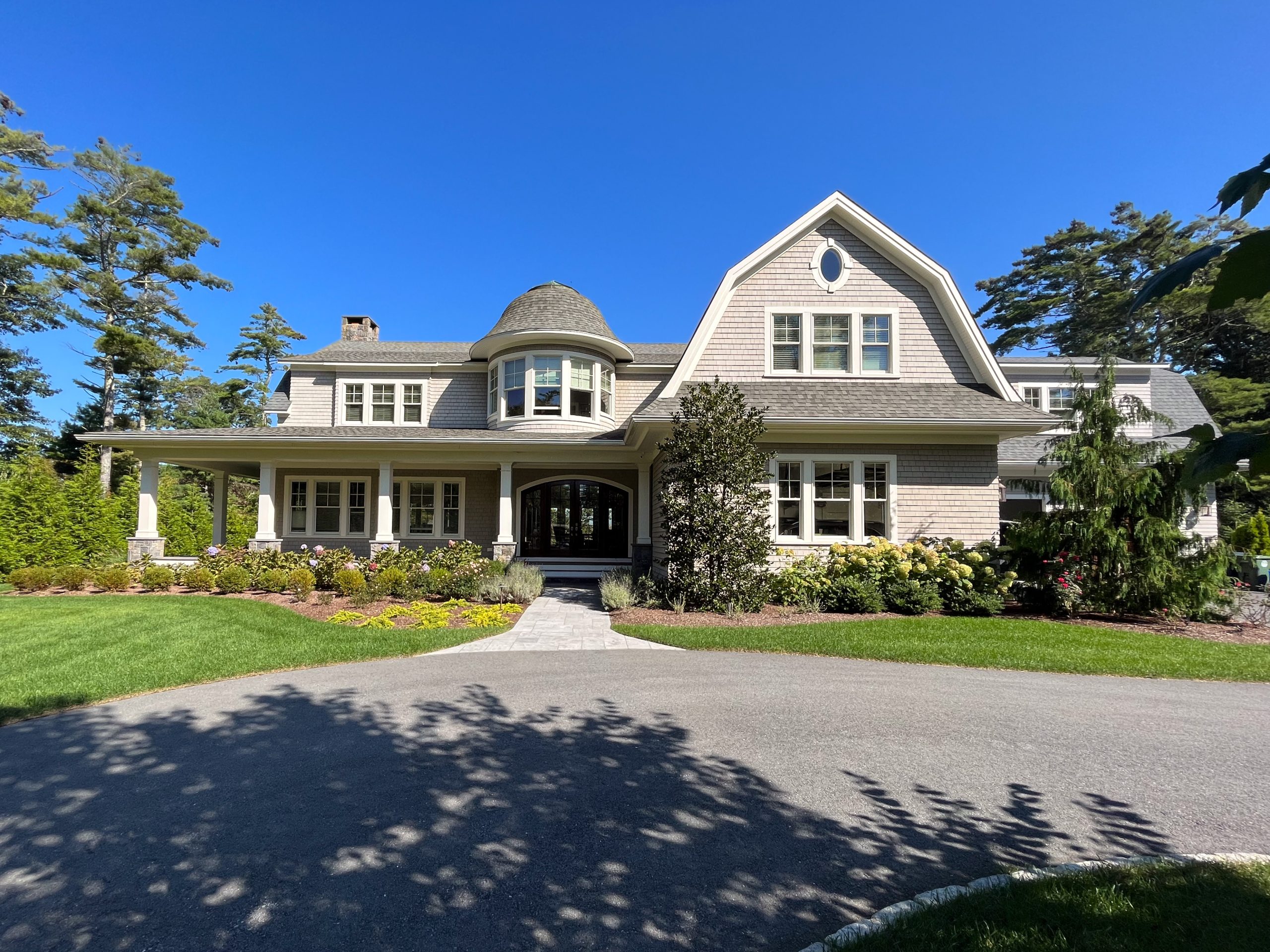 A beautiful home with peaked roof and columned porch surrounded by a green lawn and trees.