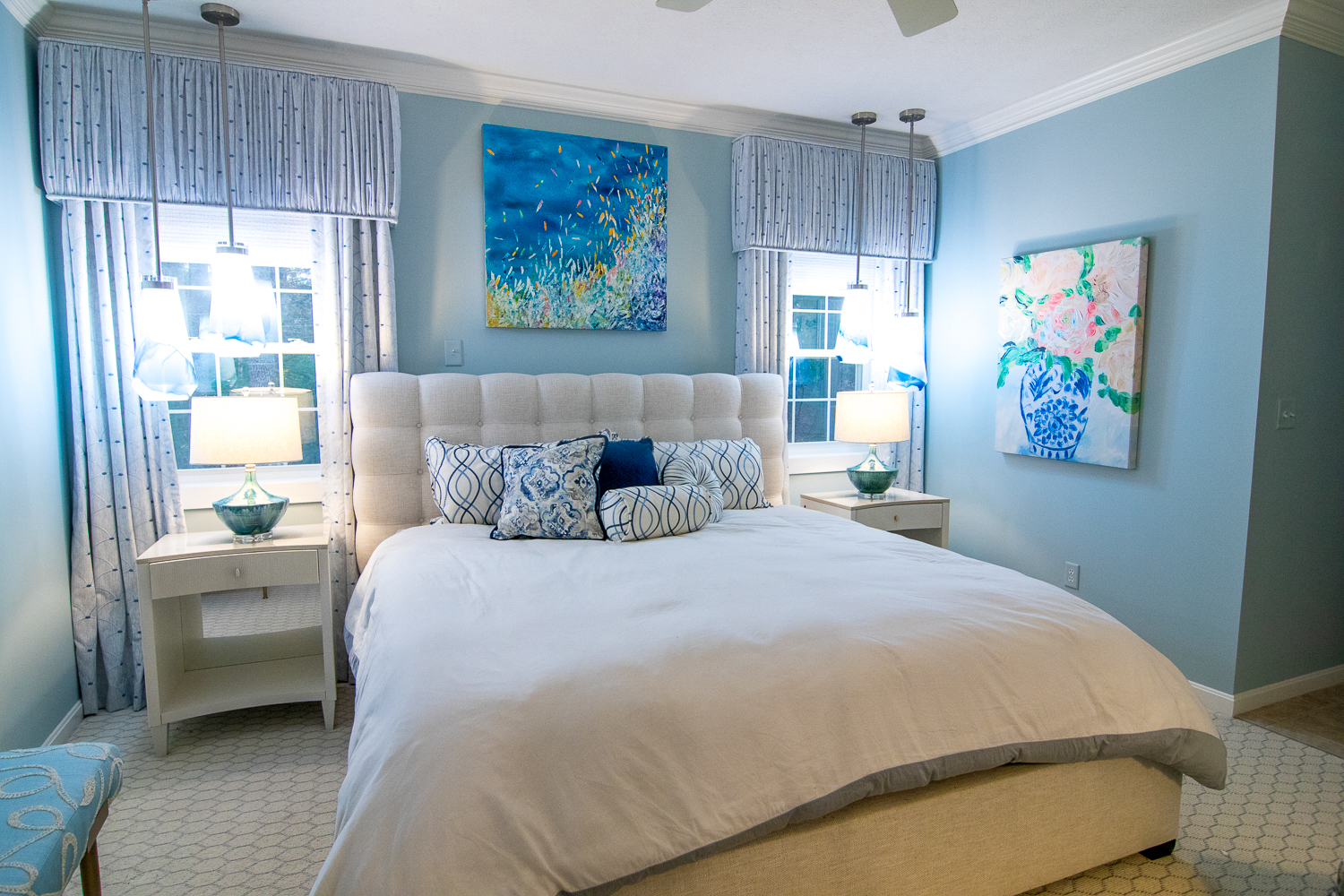 A bedroom with blue painted walls, blue and white drapes, a bed with a white upholstered headboard and white bedding